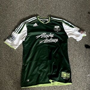 An Green Adidas shirt with Alaska airlines written on it.